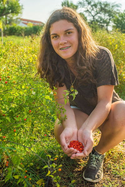 Girl with a handful of red seeds sitting in a field.